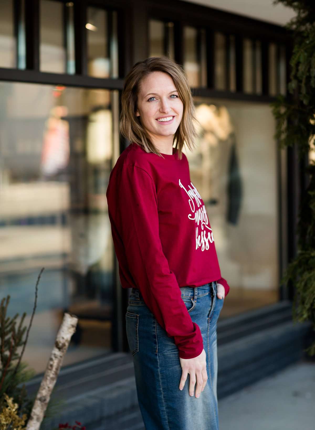 Woman standing out side of Inherit Clothing Company wearing a red and black, Joyful, Merry + Blessed Graphic Long Sleeve Tee.