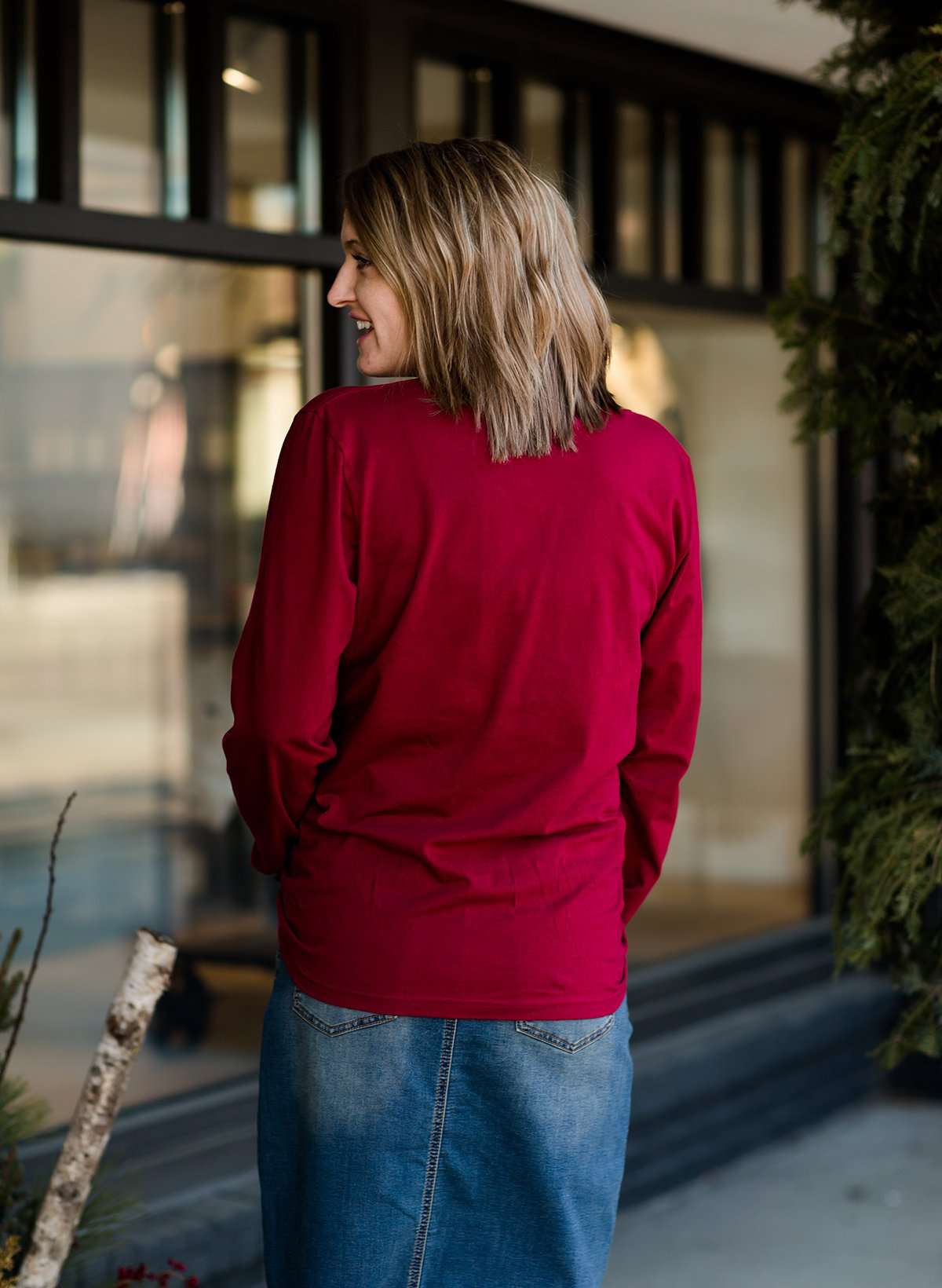 Woman standing out side of Inherit Clothing Company wearing a red and black, Joyful, Merry + Blessed Graphic Long Sleeve Tee.