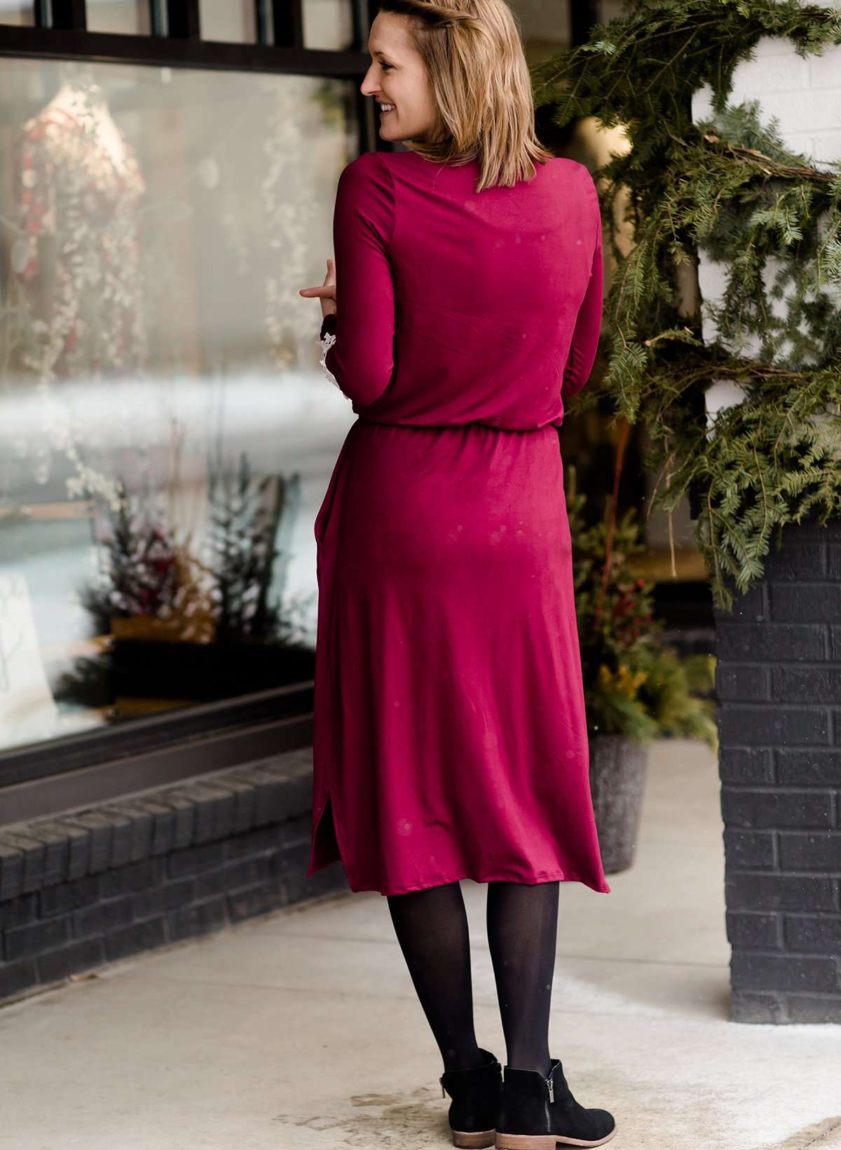 Woman wearing a burgandy and lace midi dress with black tights and sole society back boots. She is standing outside of Inherit Clothing Company.