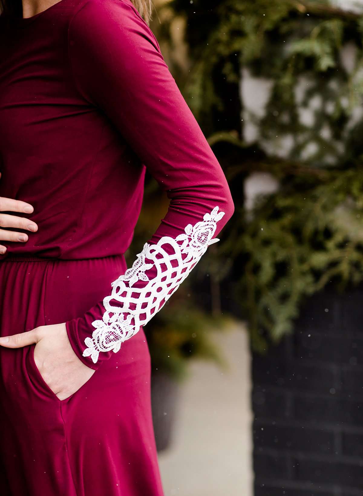 Woman wearing a burgandy and lace midi dress with black tights and sole society back boots. She is standing outside of Inherit Clothing Company.