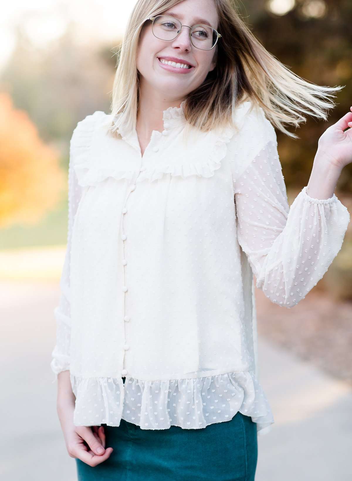 Young woman wearing a vintage inspired ruffle and layered cream colored blouse. This blouse features ruffles and ribbon details.