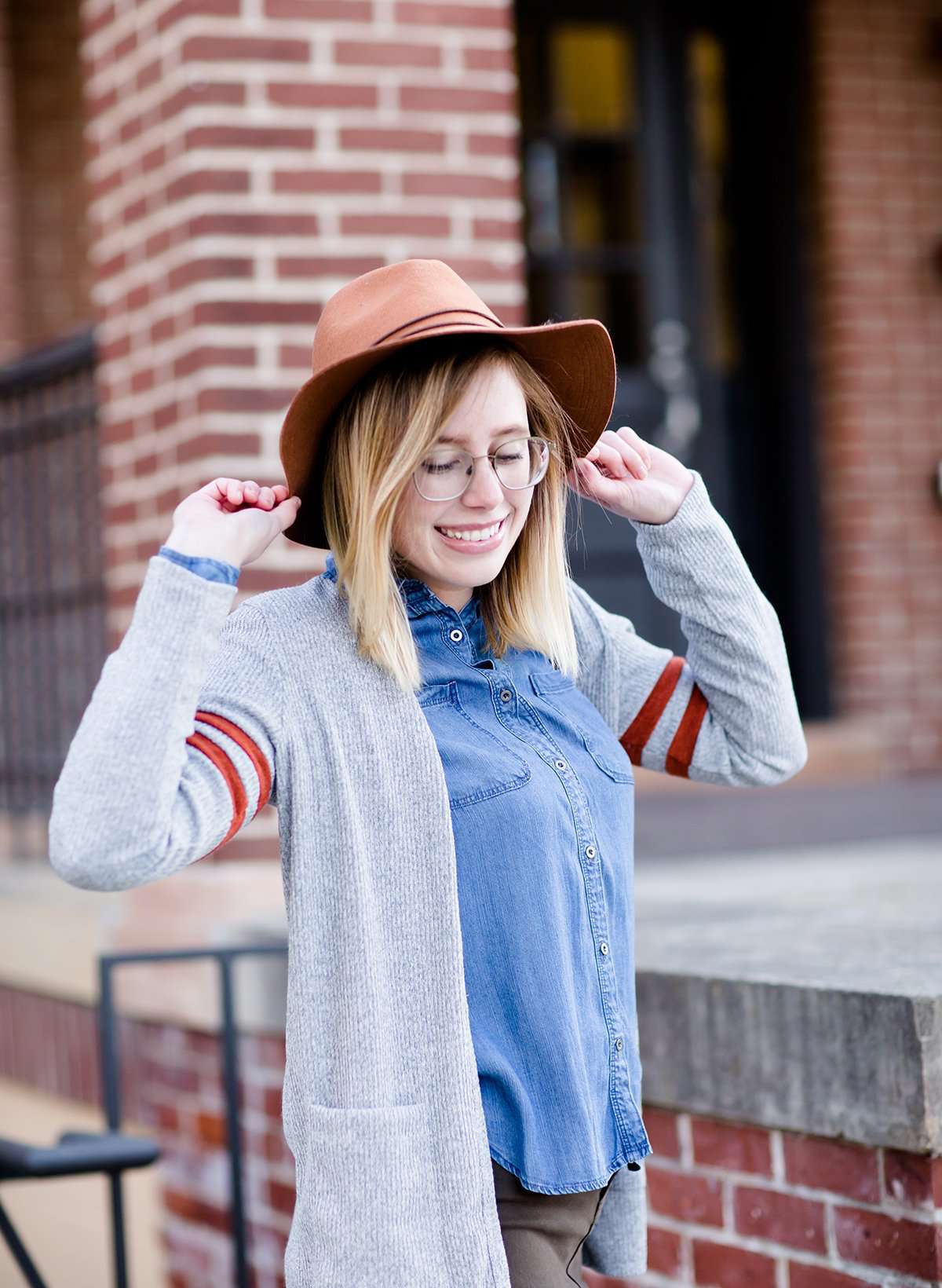 Young woman in hat and skirt wearing a gray open front long knit cardigan with orange stripes on the upper sleeve