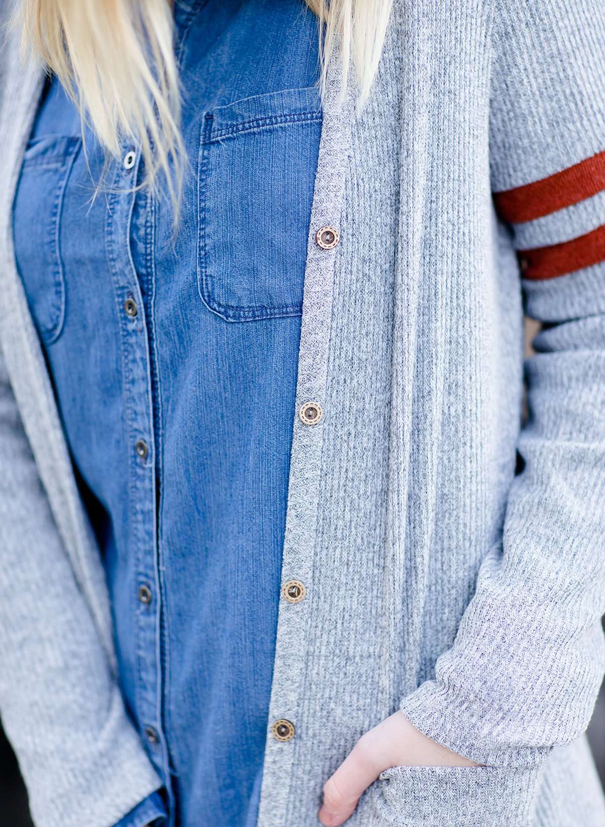 Young woman in hat and skirt wearing a gray open front long knit cardigan with orange stripes on the upper sleeve