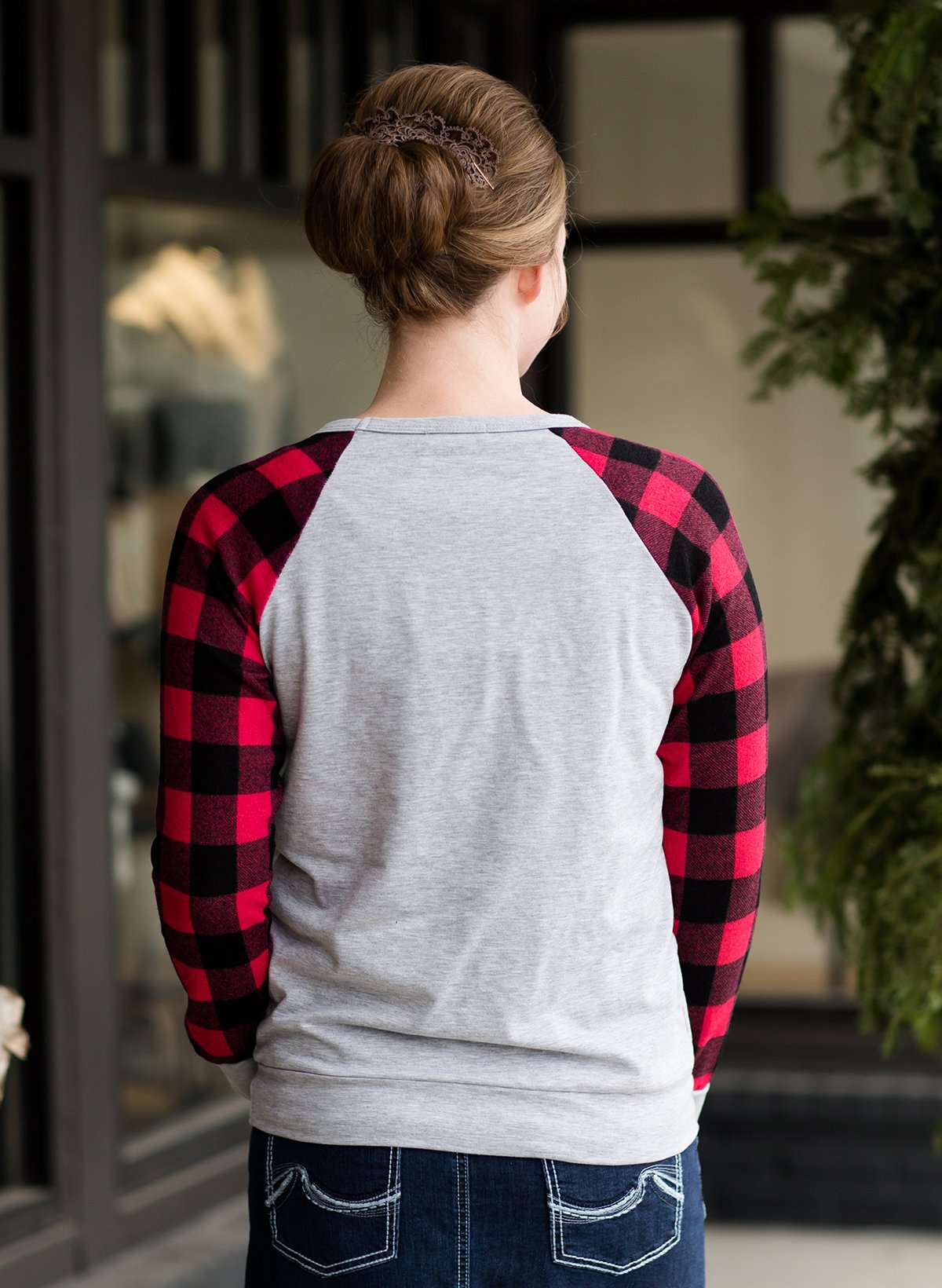 Model woman wearing a grey long sleeve tee with buffalo plaid sleeves and the script font that reads Merry Christmas.