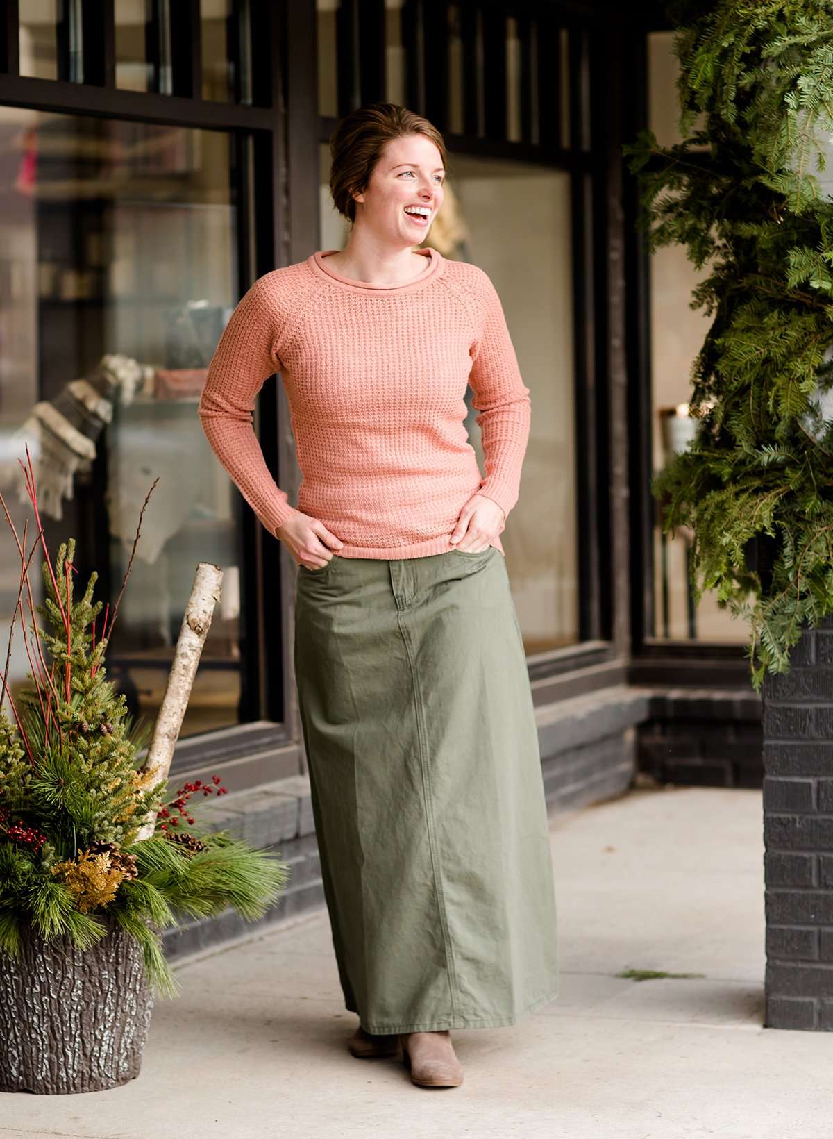 Woman wearing an olive, long modest cotton skirt. This skirt has no slit and is paired with a mauve sweater.