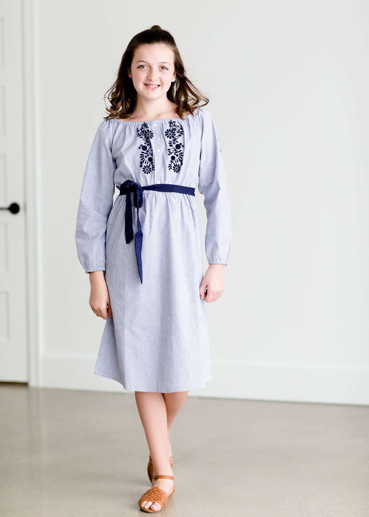 Tween wearing a navy boho pin stripe peasant dress with a self tie belt