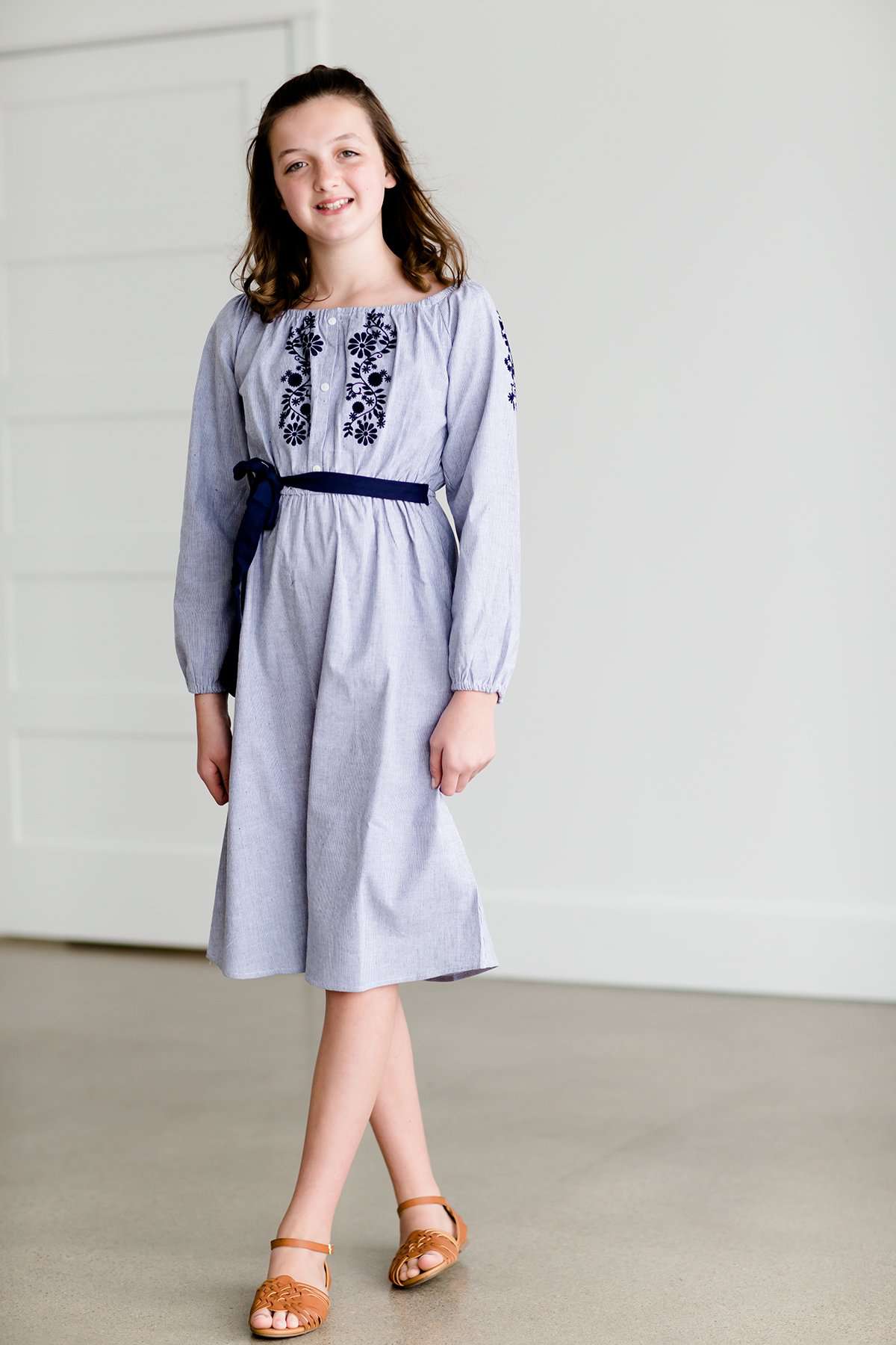 Tween wearing a navy boho pin stripe peasant dress with a self tie belt