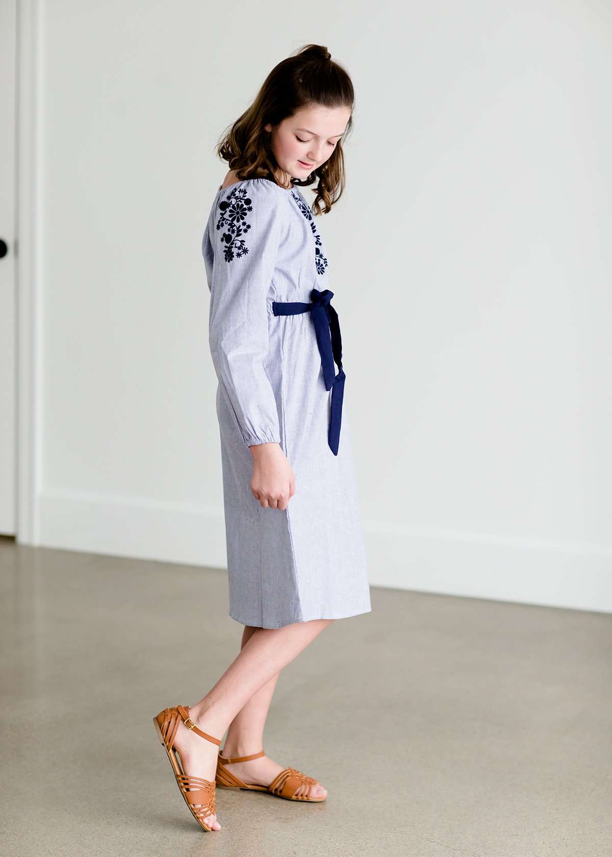 Tween wearing a navy boho pin stripe peasant dress with a self tie belt