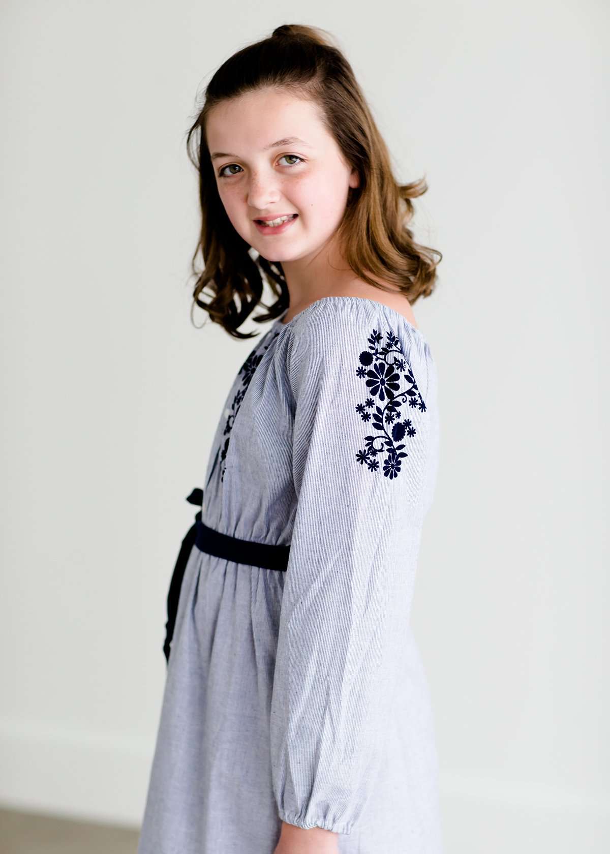 Tween wearing a navy boho pin stripe peasant dress with a self tie belt