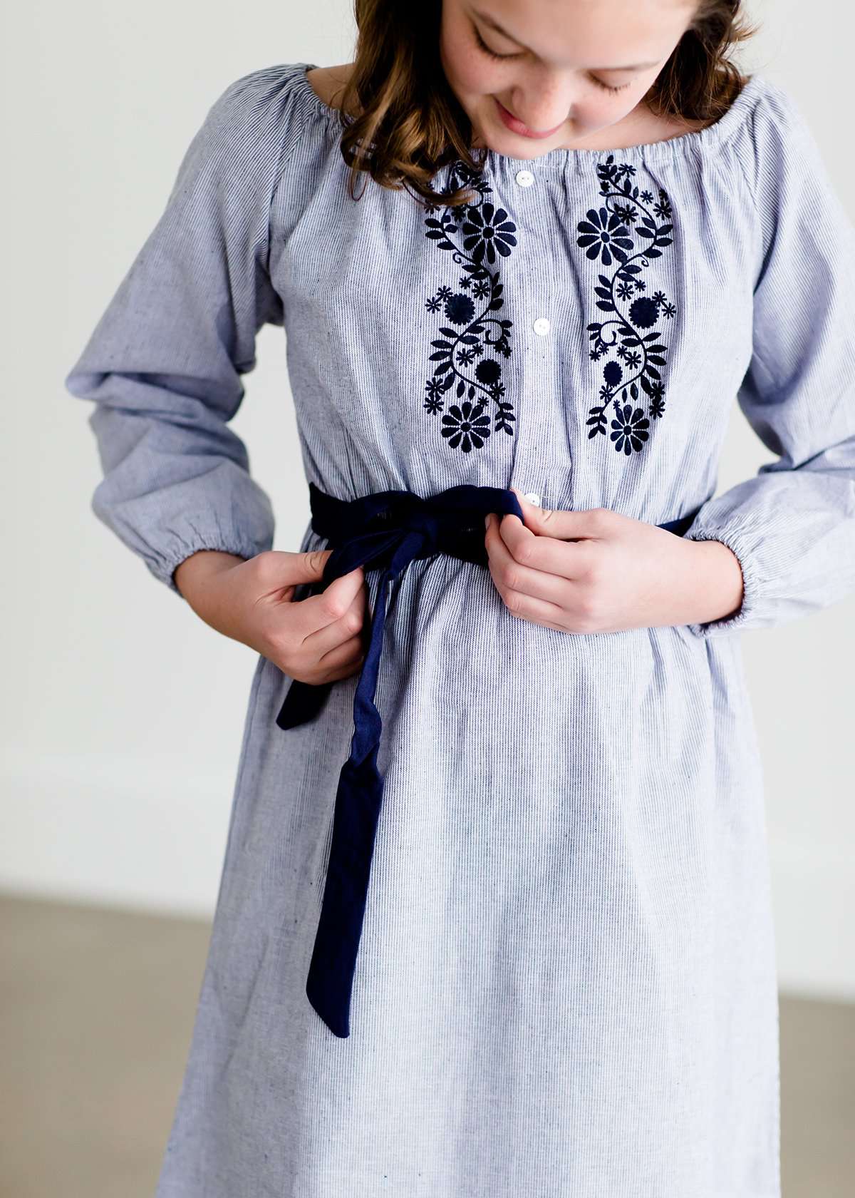 Tween wearing a navy boho pin stripe peasant dress with a self tie belt