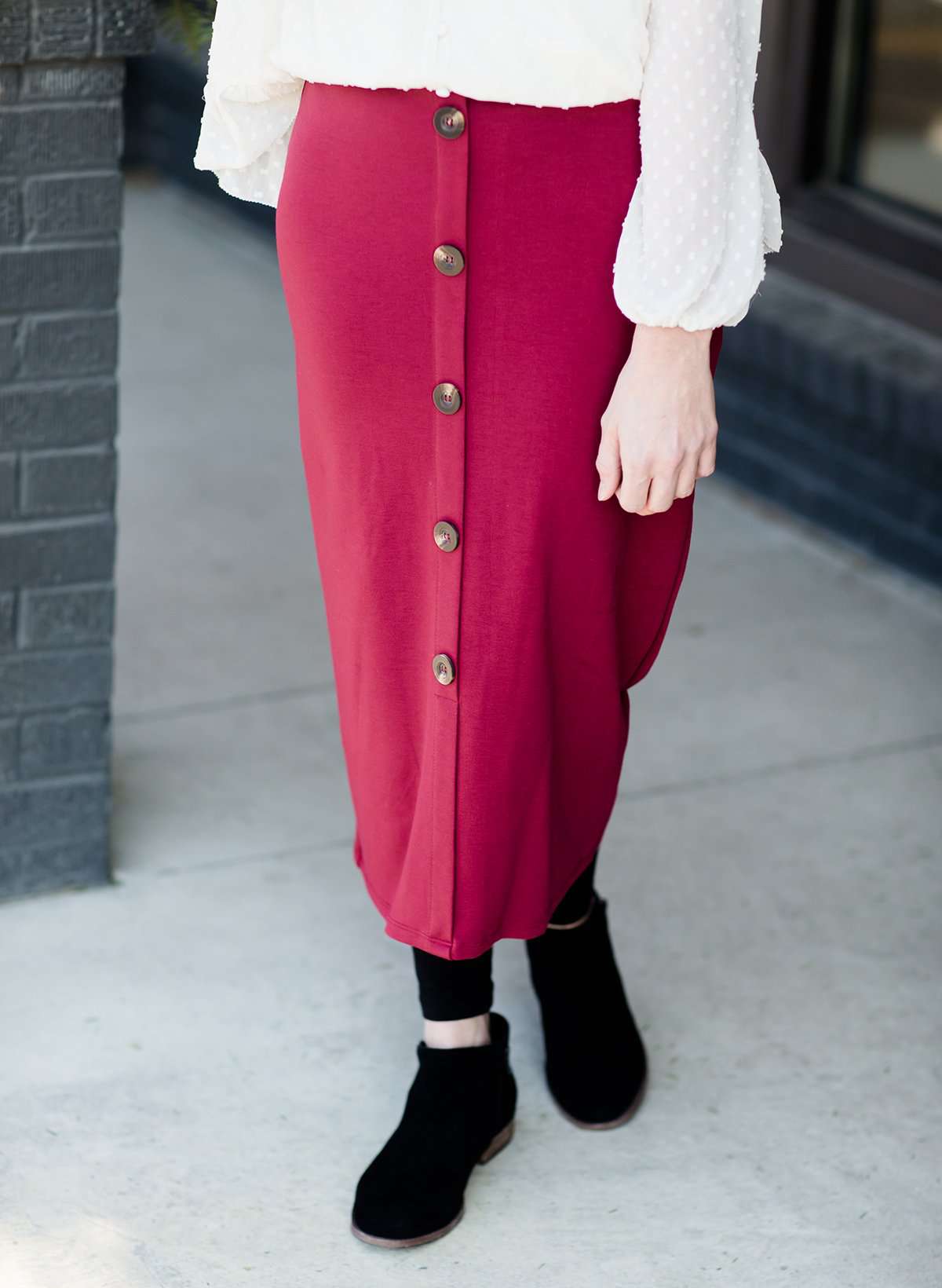 Modest below the knee wine colored skirt. This skirt has faux buttons and is paired with a white blouse and black boots.