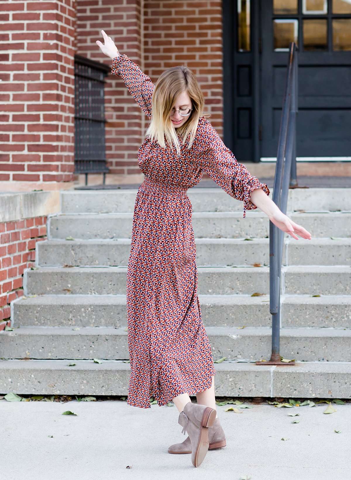 Woman on staircase wearing a rust colored, geometric print, smock maxi dress.