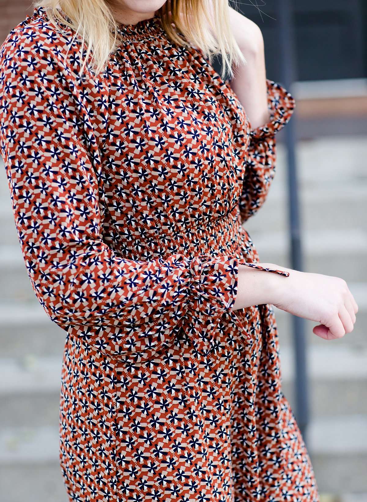 Woman on staircase wearing a rust colored, geometric print, smock maxi dress.