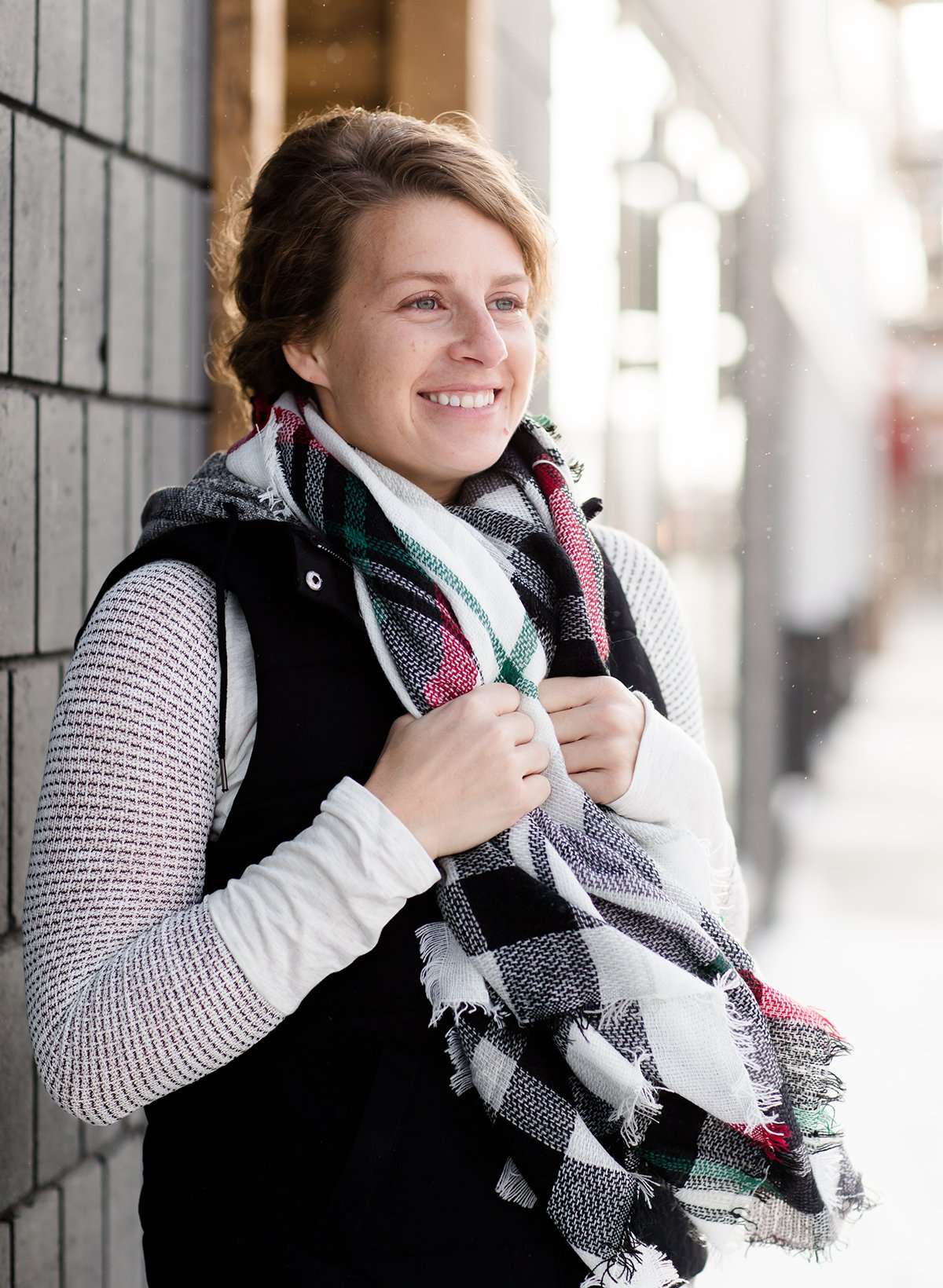 Woman wearing an anorak quilted vest with a zipper and hood. This vest comes in olive or black with gray accents.