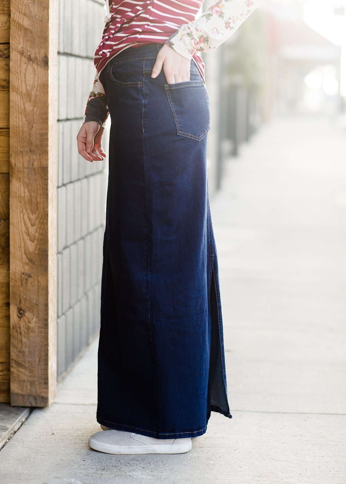 Woman wearing a long denim jean skirt that has a dark wash and a light wash. this is a long modest jean skirt.