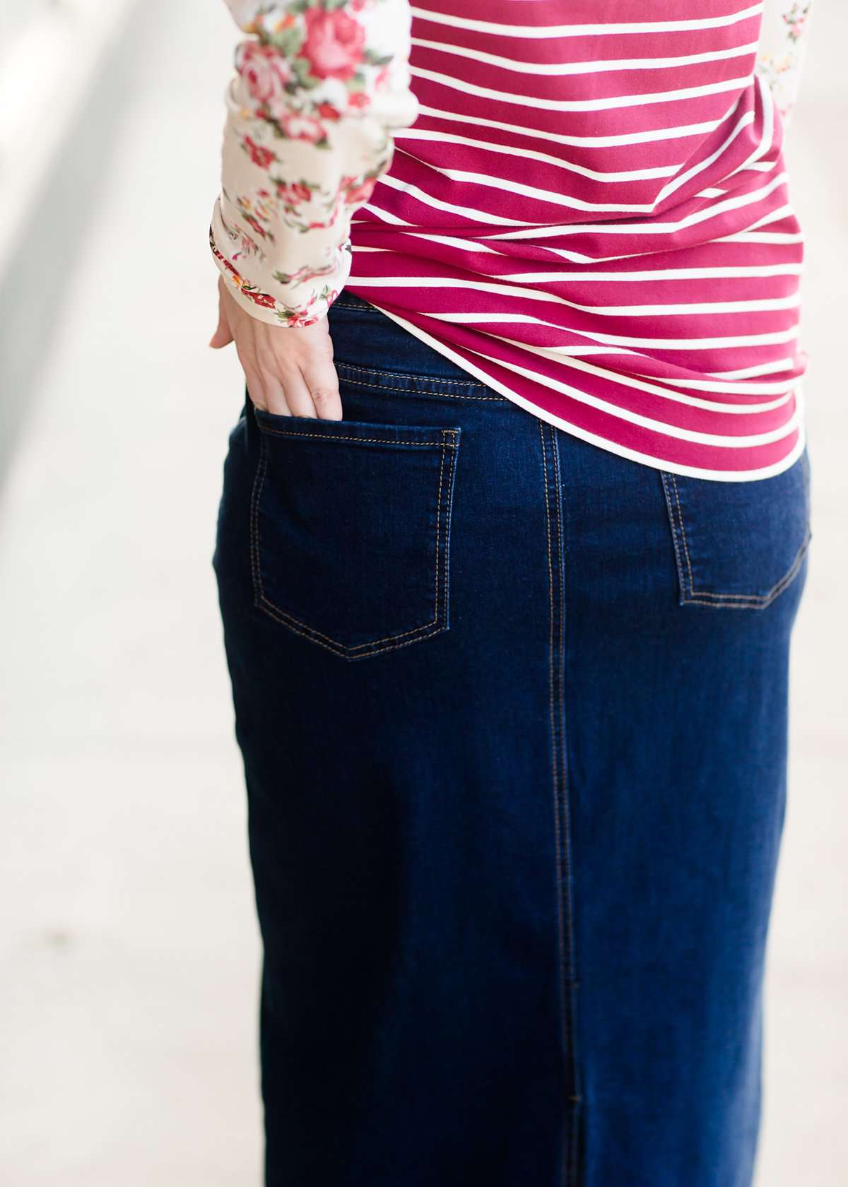 Woman wearing a long denim jean skirt that has a dark wash and a light wash. this is a long modest jean skirt.