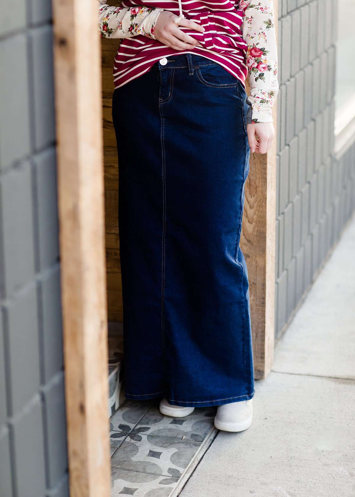Woman wearing a long denim jean skirt that has a dark wash and a light wash. this is a long modest jean skirt.