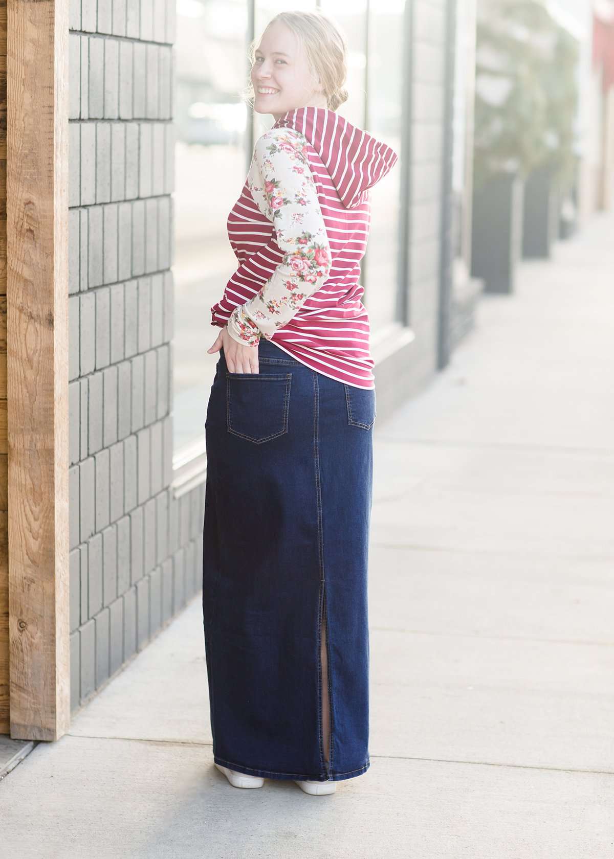 Woman wearing a long denim jean skirt that has a dark wash and a light wash. this is a long modest jean skirt.