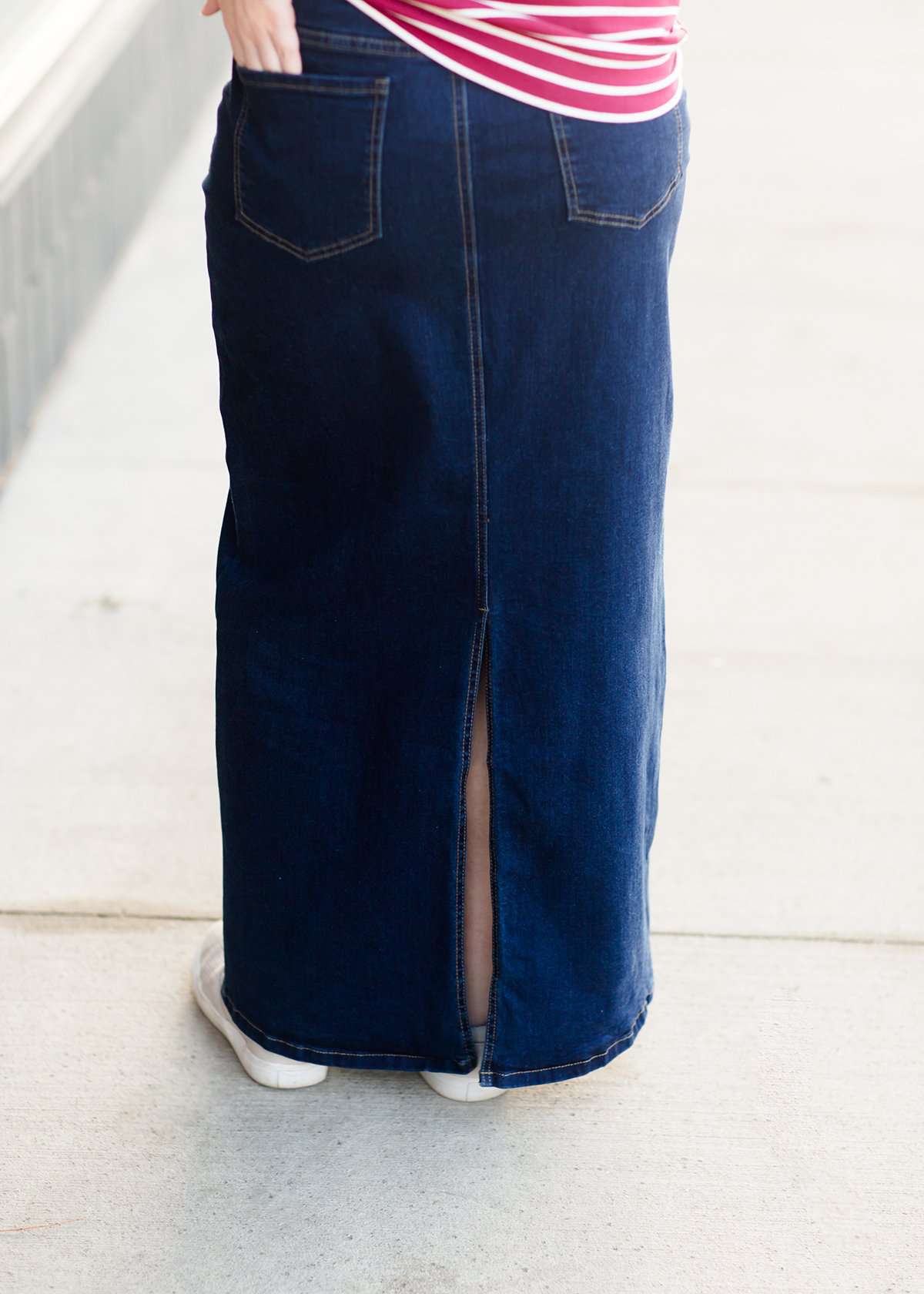 Woman wearing a long denim jean skirt that has a dark wash and a light wash. this is a long modest jean skirt.
