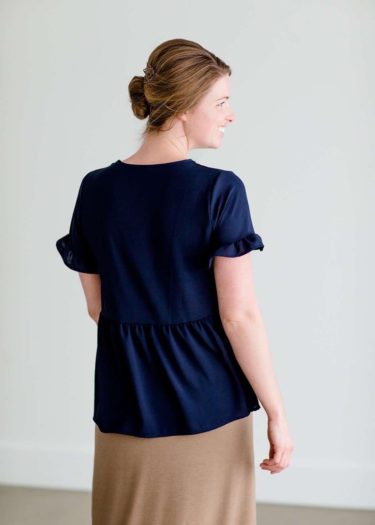 Woman wearing a navy peplum baby doll top that has ruffle details on the sleeves.