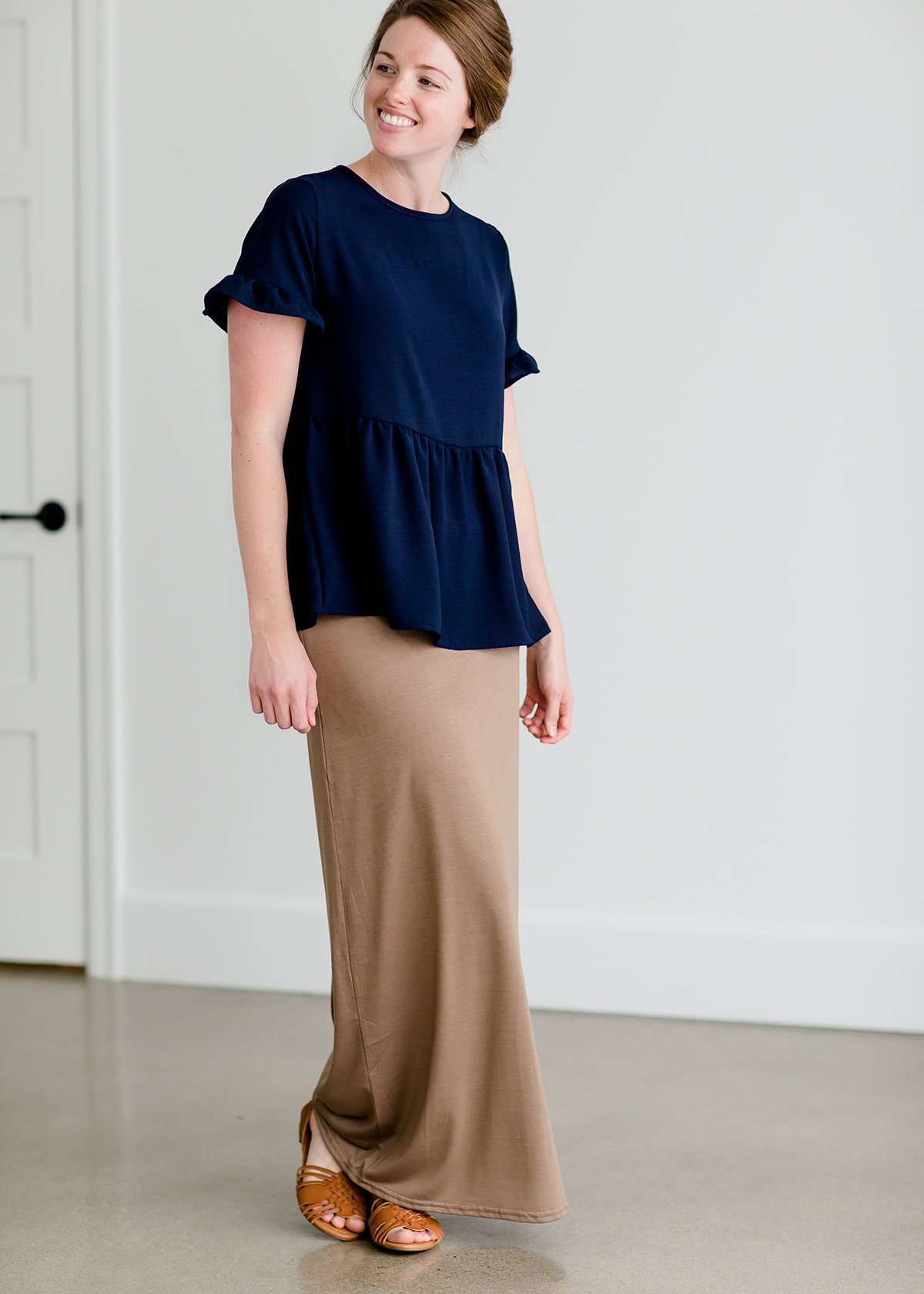 Woman wearing a navy peplum baby doll top that has ruffle details on the sleeves.