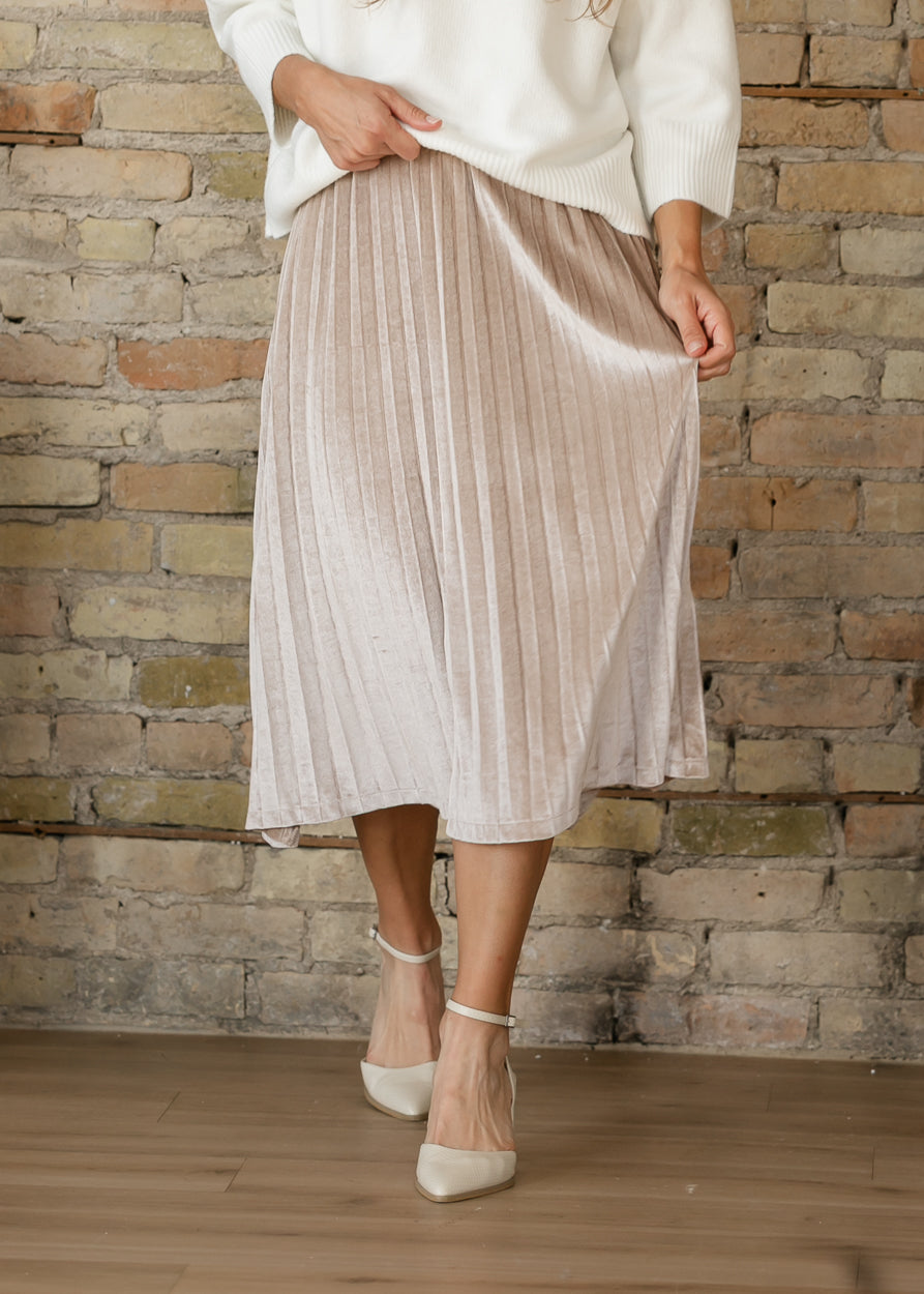 Front of tan pink velvet midi skirt showing its soft sheen, narrow pleats, and gently flared silhouette.