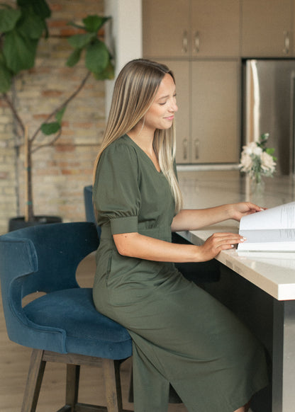 Seated side view of the olive green midi dress showing the V-neckline and gathered waist.