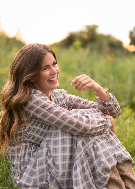 Taupe plaid maxi dress styled with tan boots, seated among wildflowers at sunset.