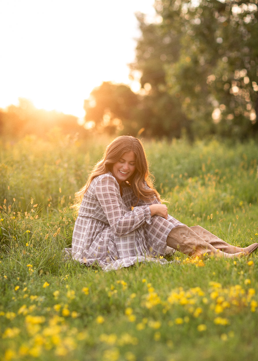 Taupe plaid maxi dress styled with tan boots, seated among wildflowers at sunset.