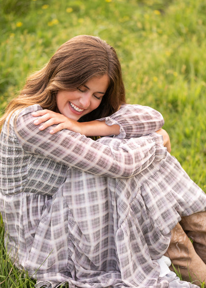 Taupe plaid maxi dress styled with tan boots, seated among wildflowers at sunset.