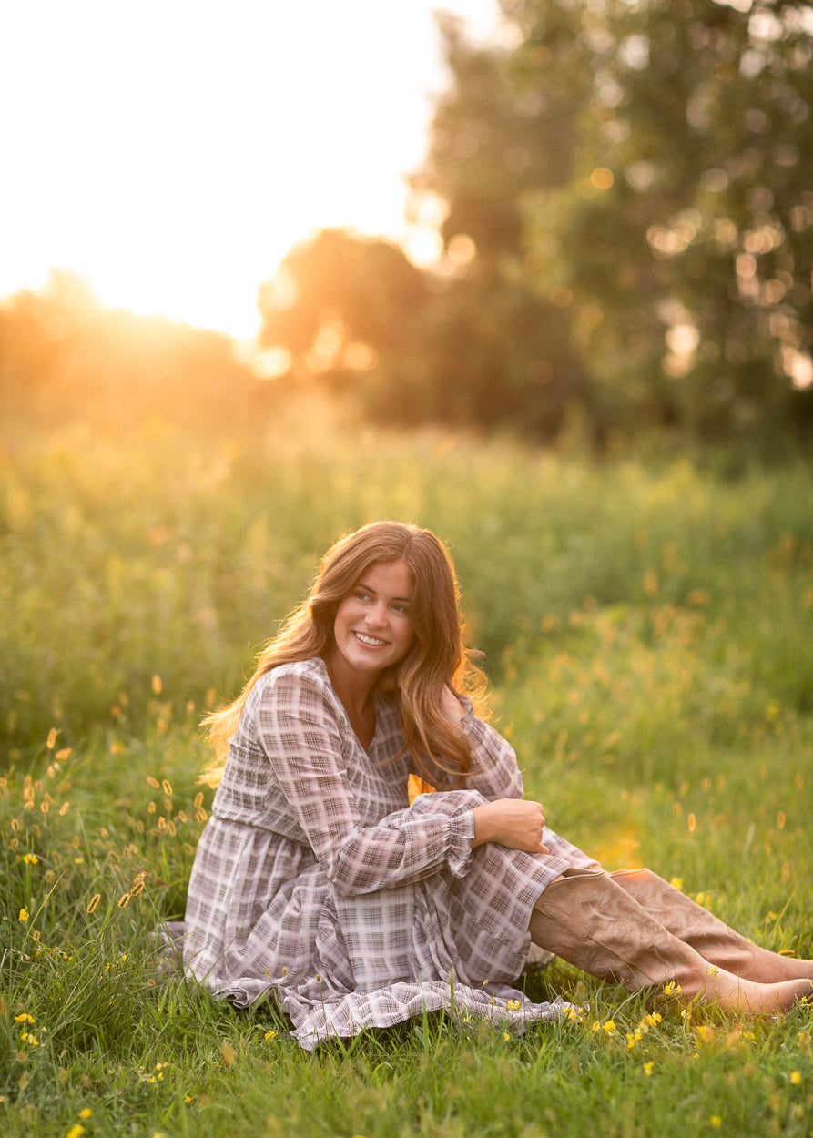 Taupe plaid maxi dress with smocked bodice detail, seated outdoors at golden hour.