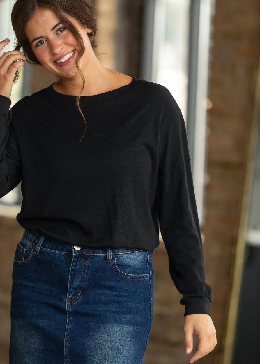 Black long sleeve top with a loose fit, styled with a dark wash denim maxi skirt and neutral shoes.
