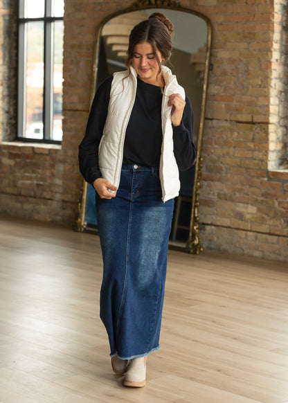 Black long sleeve top styled with a cream vest and dark wash denim maxi skirt beside a neutral top.