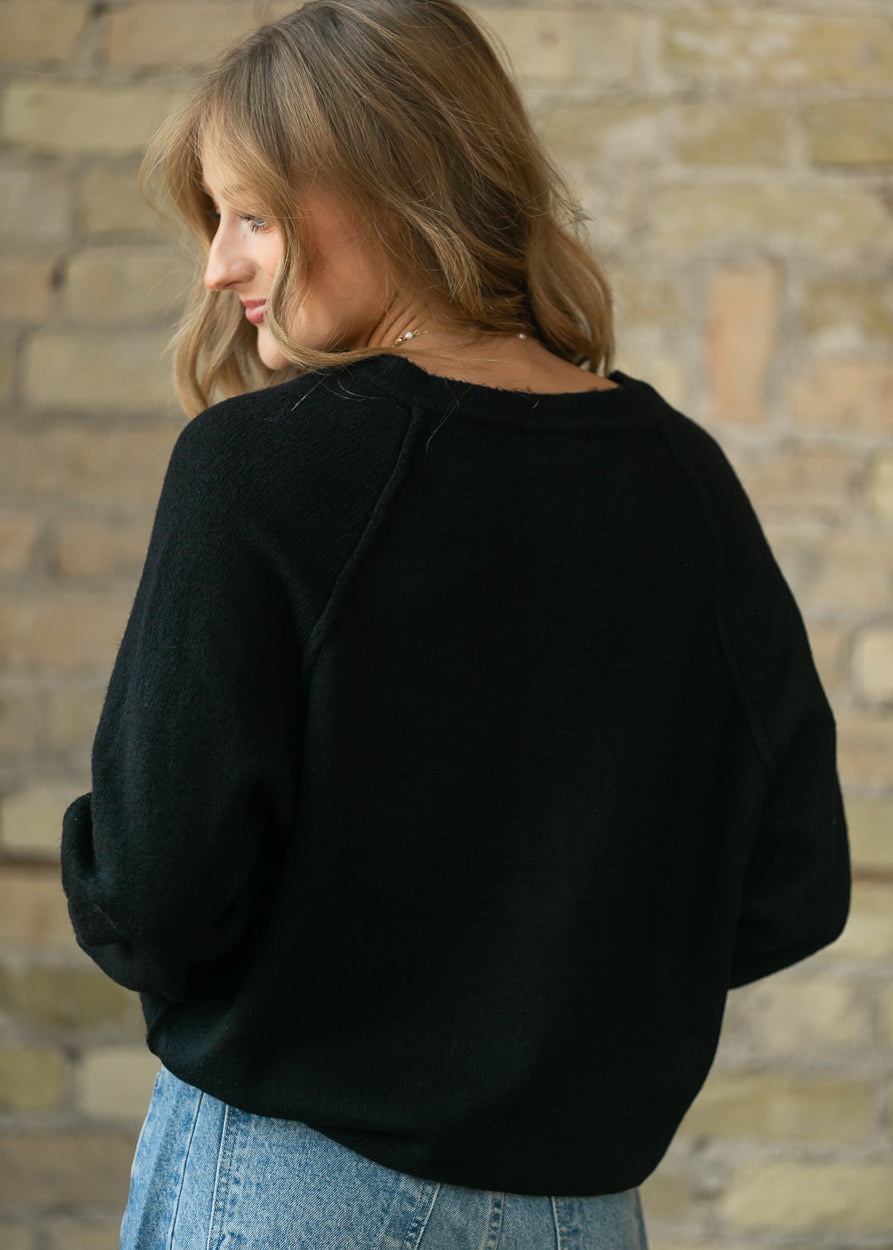 Back of the black henley sweater showing raglan sleeves and a relaxed, hip-length fit.