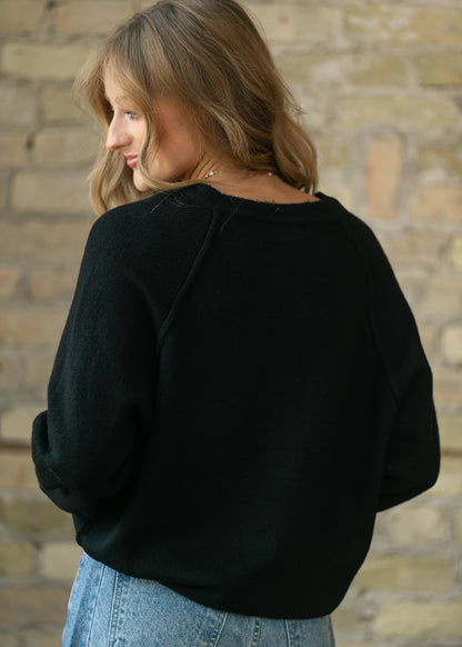 Back of the black henley sweater showing raglan sleeves and a relaxed, hip-length fit.