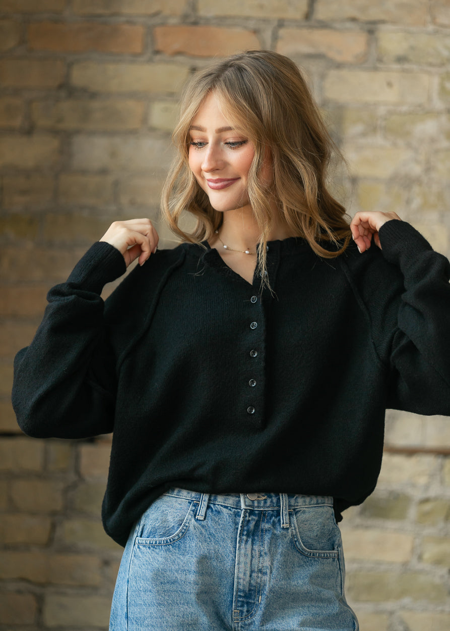 Close-up of the black henley sweater's button placket and raw-edge neckline detail.