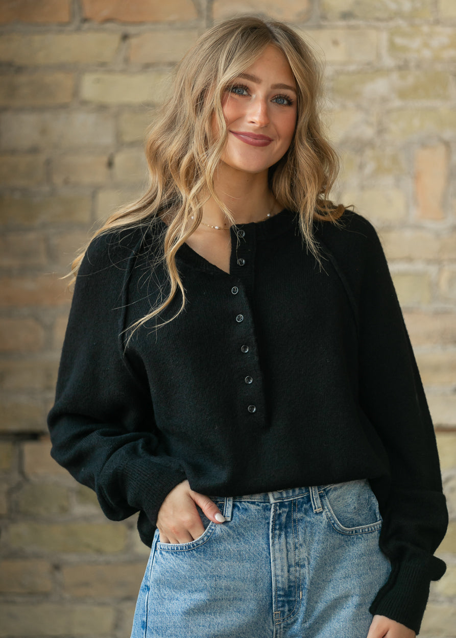 Close-up of the black henley sweater's button placket and raw-edge neckline detail.