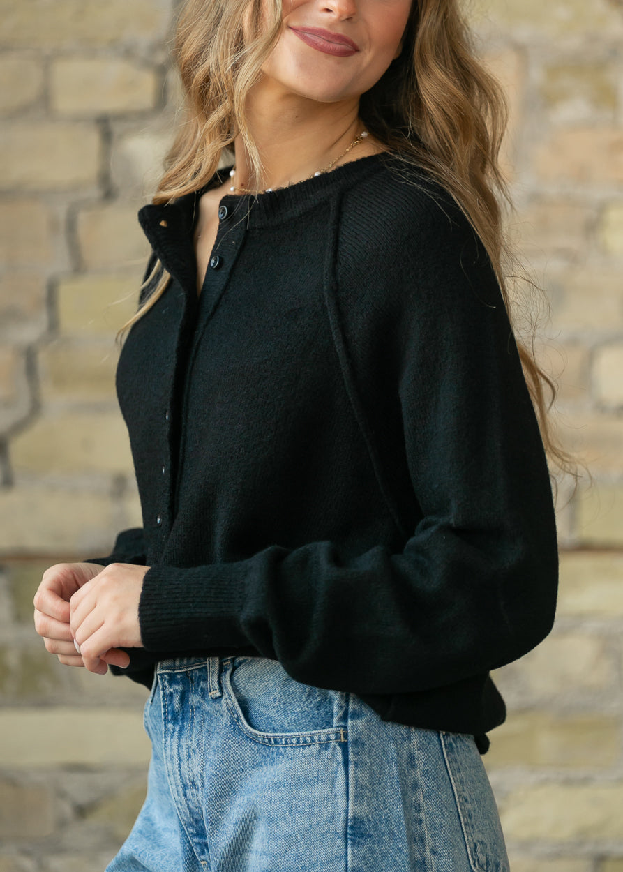 Close-up of the black henley sweater's button placket and raw-edge neckline detail.