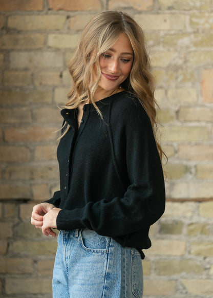 Close-up of the black henley sweater's button placket and raw-edge neckline detail.
