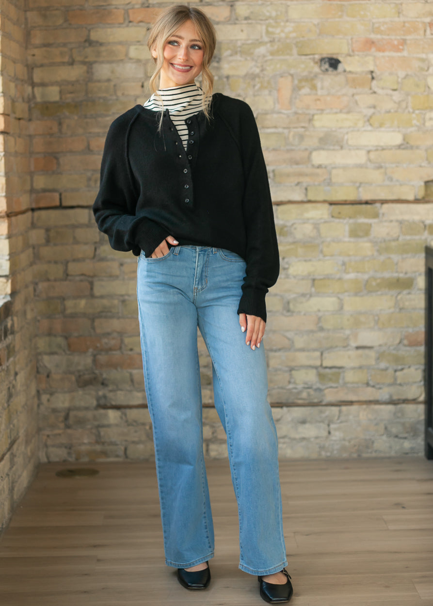 Front view of the black henley sweater layered over a striped turtleneck and denim jeans.