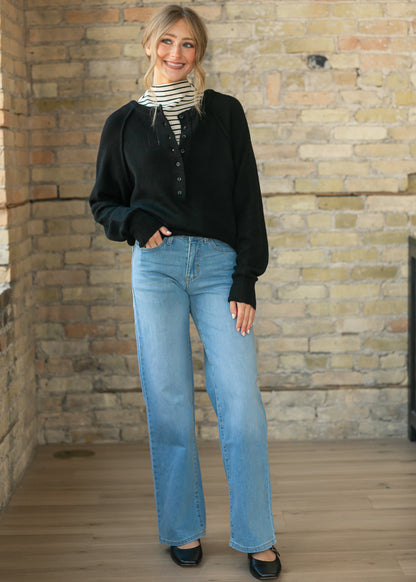 Front view of the black henley sweater layered over a striped turtleneck and denim jeans.