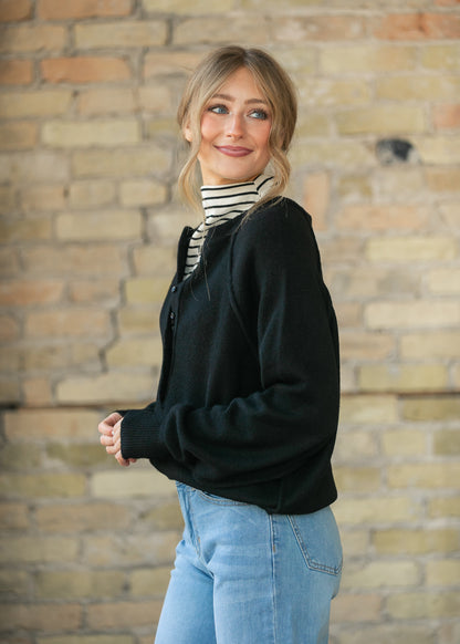 Black henley sweater layered over a striped turtleneck, styled with wide-leg denim and black flats.