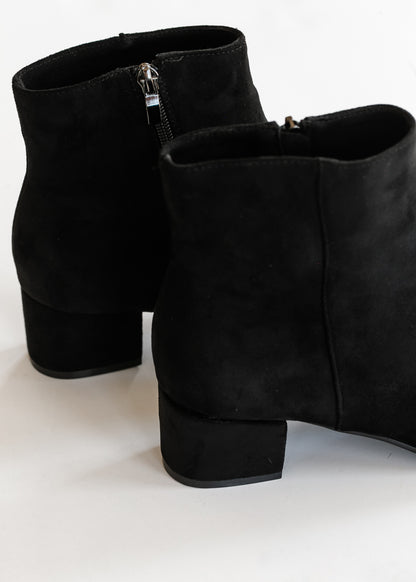 Close-up of black ankle boot showing soft matte texture, pointed toe, and side zipper.