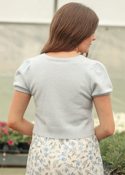 Back view of heathered blue cardigan with short puff sleeves and ribbed hem, styled with a blue floral maxi skirt.
