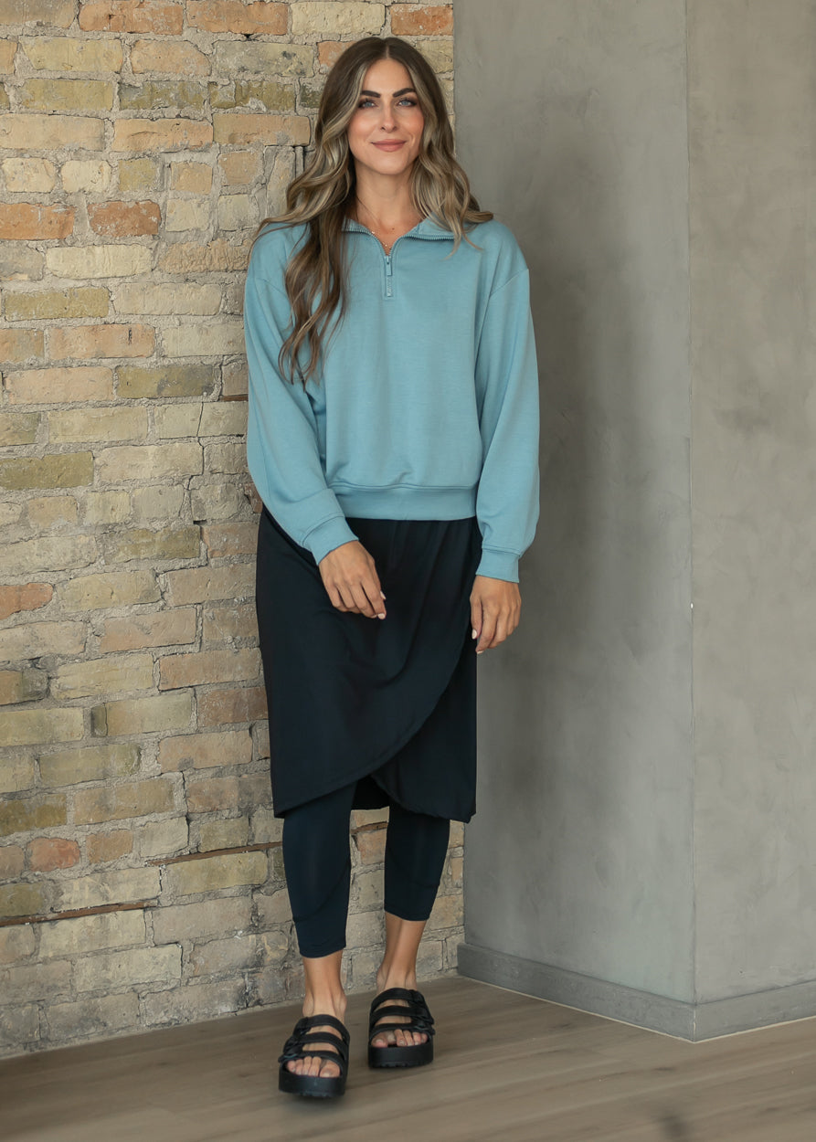 Blue-gray quarter-zip sweatshirt styled with a black skirt and platform sandals, front view.