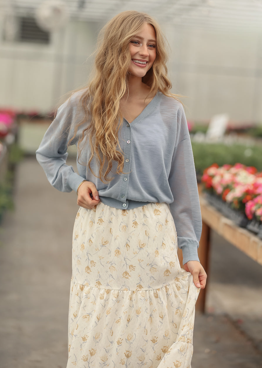 Blue cropped cardigan layered over a cream floral maxi skirt with neutral accessories