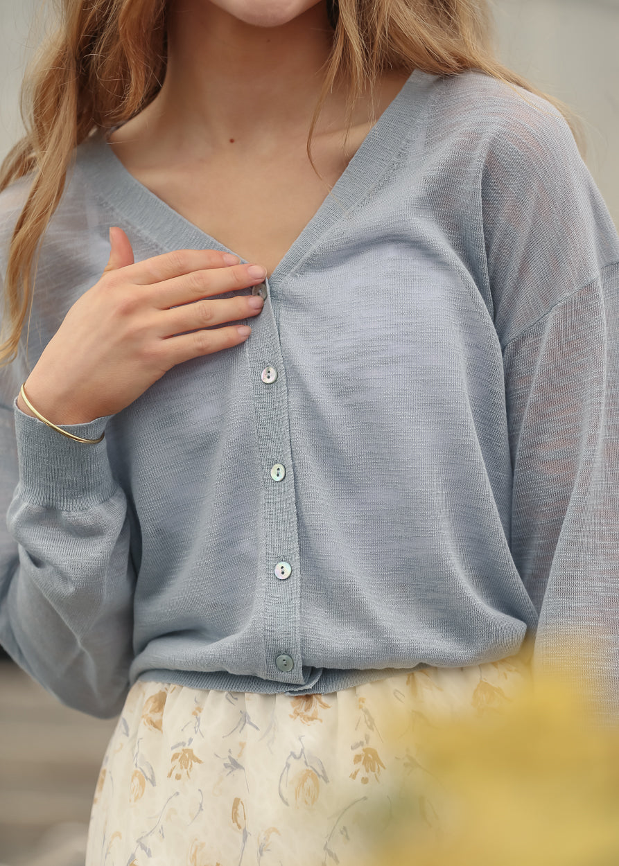 Close-up of blue sheer knit cardigan with functional buttons and ribbed cuffs