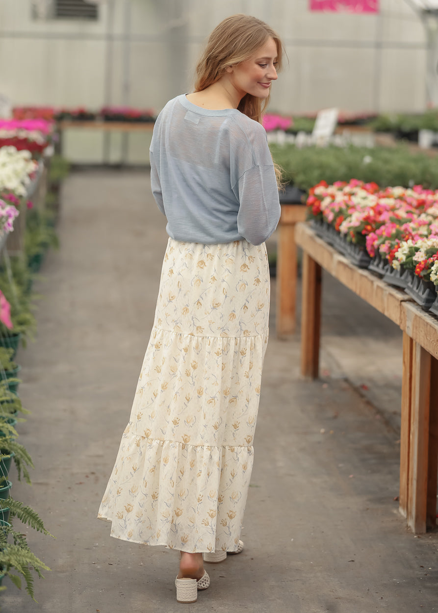 Back view of blue lightweight cardigan layered over a cream floral tiered maxi skirt