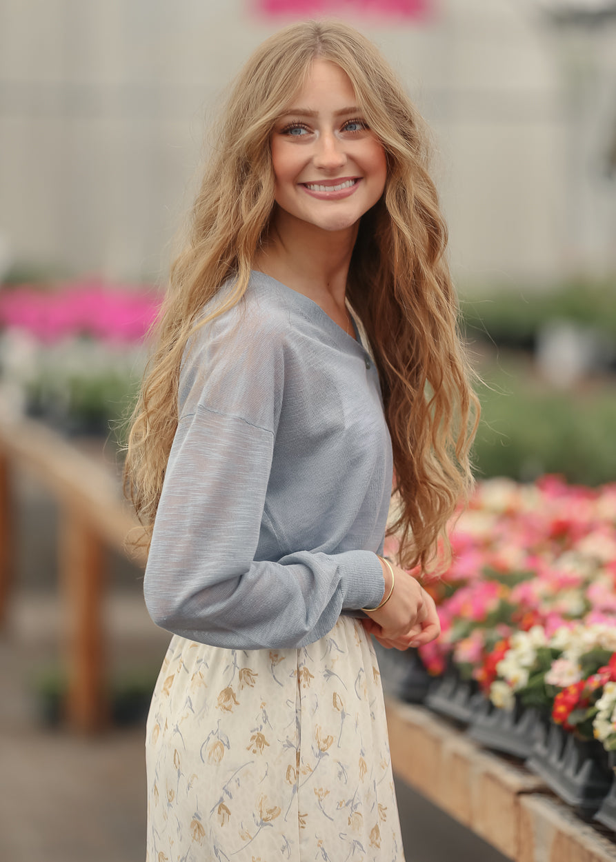 Dusty blue lightweight cardigan styled with a cream floral maxi skirt in a greenhouse