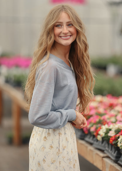 Dusty blue lightweight cardigan styled with a cream floral maxi skirt in a greenhouse